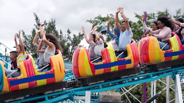 Happy group of people having fun in an amusement park riding on a rollercoaster with arms up
